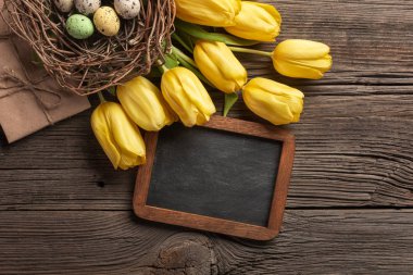 Sarı laleler bir kağıt torba, bir ahşap arka plan üzerinde bir yuva ile Paskalya yumurta. Kopya alanı ile üstten görünüm.