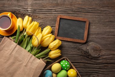 Sarı laleler bir kağıt torba, bir ahşap arka plan üzerinde bir yuva ile Paskalya yumurta. Kopya spacev ile Üstten Görünüm.