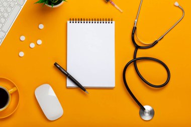 Tablonun bir doktorun not defteri ve kalem stetoskop, klavye, reçete ve ilaç, bir fincan kahve sarı bir arka plan üzerinde Üstten Görünüm