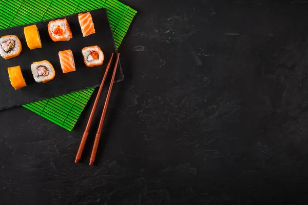 Palillos de sushi japoneses sobre un tazón de salsa de soja, arroz sobre fondo de piedra negra. Vista superior con espacio de copia —  Fotos de Stock