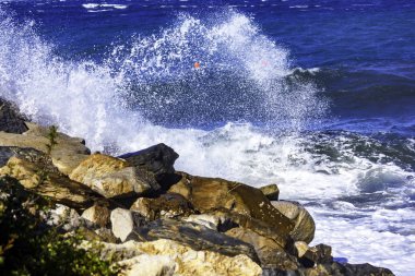 koyu mavi monotonluğu içinde sörf sallamak kıyıda haddelenmiş. Köpük beyaz, kapalı sarı kum ve iri taşlar sprey