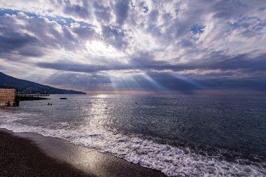 Yükselen güneşin parlak ışınları bulutları güneş ışığı iğneleriyle delip geçiyor ve güzel bir şekilde denizde küçük dalgaları aydınlatıyor.