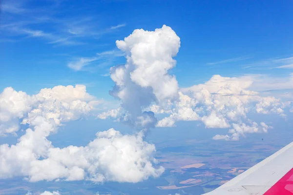 Under the wing of the plane, white fluffy and dark gloomy clouds float by, changing their color from the desire of the sun