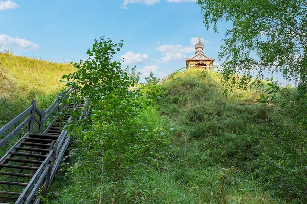 Tepede haçı olan eski ahşap bir şapel çürük korkuluklu ahşap bir merdivenle ulaşılır.