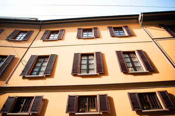 Yellow wall with brown windows with shutters, European living house facade, low angle view