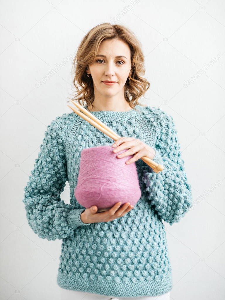 Pretty young woman knits woolen clothes. Girl with knitting needles and wool yarn