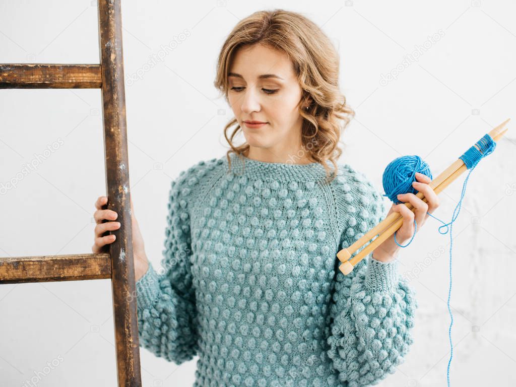 Pretty young woman knits woolen clothes. Girl with knitting needles and wool yarn