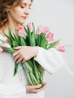 Pembe lale güzel bir demet gün ışığı ile beyaz duvara onun elinde tutan genç kadın. Anneler günü kutlama kavramı, buket çiçekler.