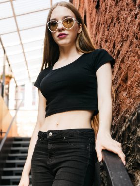 Siyah aşınma ve güneş gözlüğü uzun sarı saçlı kentsel duvar boyunca yakın poz trendy rahat genç kadın portresi 