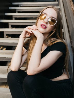 Siyah aşınma ve güneş gözlüğü uzun sarı saçlı kentsel duvar boyunca yakın poz trendy rahat genç kadın portresi 