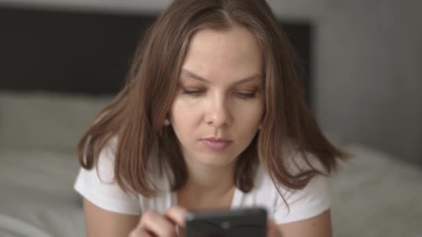 Kvinna liggande på sängen med hjälp av smartphone hemma i sovrummet — Stockvideo