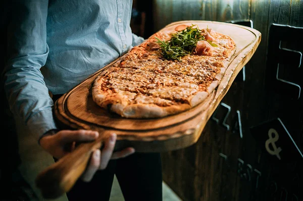 Garson pizza var. Bir ahşap tepsi garsonun ellerini tutun. 