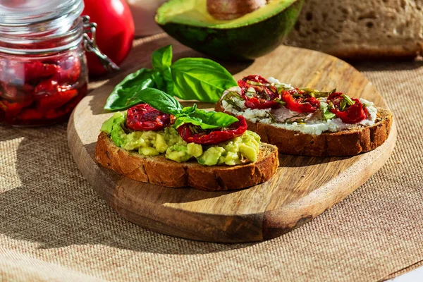 Sandwich with sun-dried tomatoes, avocado, basil, curd cheese on croutons. Vegetarian breakfast or snack.