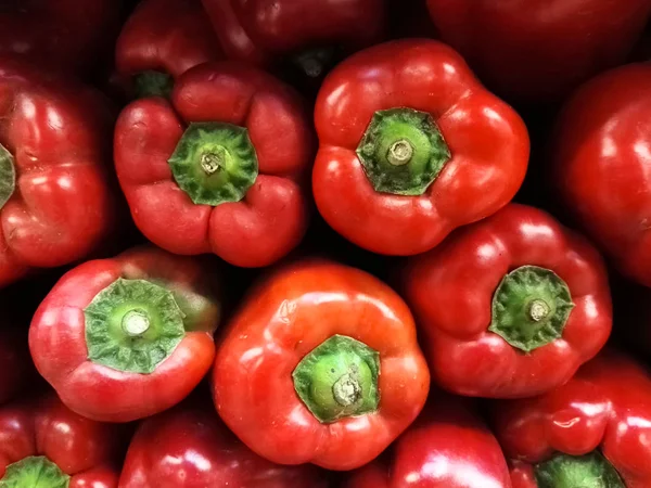 Delicious and bright red bell peppers stacked on a shelf of a supermarket. View of the top part of this vegetable.