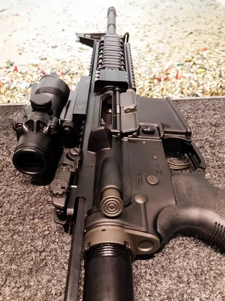 Black rifle gun with a big scope located on a shooting range with a lot of bullet casings