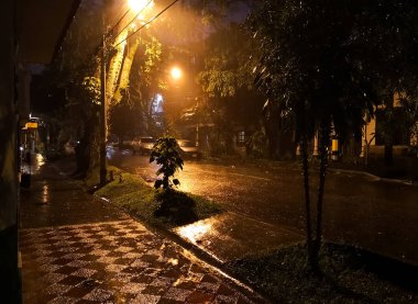 Karanlık sokak soluk sarı ışık yansımaları ile sağanak yağmur nedeniyle su ile kaplı. Fırtına ve gizemli gece