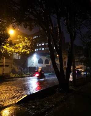 Islak ağır soluk sarı sokak ışıkları ve yüksek hızda gidecek bir motosiklet yansımaları yağmurla gelen sokak