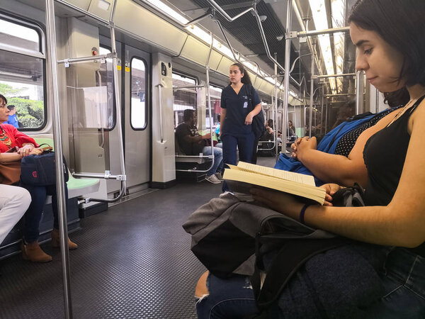 Young woman reading a book while traveling in public transport, metro. Interior of a metro car with people sitting and reading.