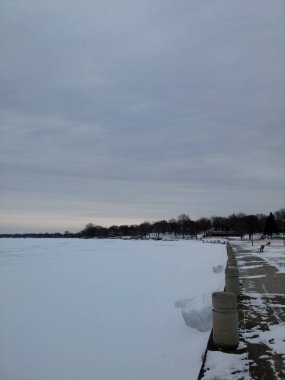Tamamen donmuş gölün kar kalın bir tabaka kaplı. Bir parka bitişik göl kenarı. Çıplak ağaçlar küçük Kent Ormanı.