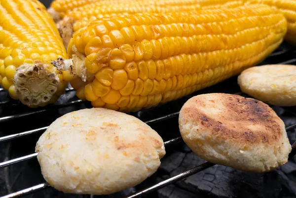 Delicious ears of corn on a grill, covered with butter and salt, ready to eat and accompanied by small Colombian arepas