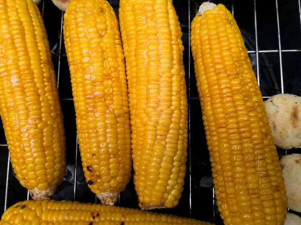 Delicious corncobs roasting on a grill, covered with butter and salt, ready to eat