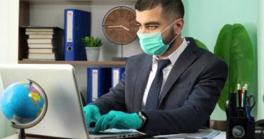 Genç işadamı masada oturuyor, Coronavirus 'un sözlerini tutuyor ve tıbbi maske ve eldivenlerle kameraya bakıyor.