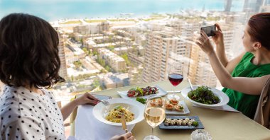 Kahvaltıda iki kadın, biri şehrin fotoğrafını çekiyor.