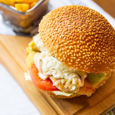 Tahta tabakta patates kızartmalı Sezar burgeri yakın.