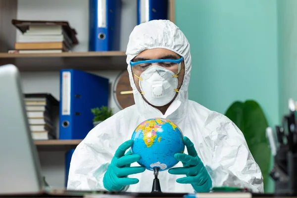 Disinfection man with special white suite holding globe earth at office