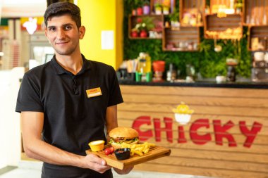 Garson elinde patates kızartması ve sosla hamburger tutuyor.