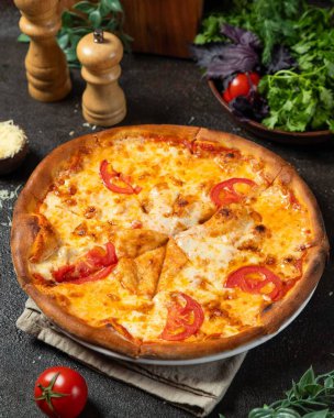 Freshly baked pizza with melted cheese and tomato slices, served on a dark table, ready to be enjoyed