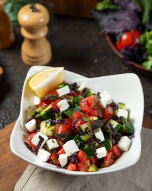 Taze domatesler, salatalıklar ve beyaz bir kasede servis edilen ve sağlıklı ve ferahlatıcı bir yemek için mükemmel olan Yunan salatası, limon ve zeytin yağıyla çeşnilendirilmiş salata.