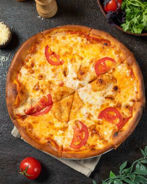 Round pizza with tomato slices and melted mozzarella cheese, resting on a dark surface, creating a tempting culinary scene