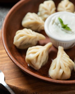 Buharda pişirilmiş Gürcü hamur köftesi, khinkali, ekşi krema ve nane ile ahşap bir tahtanın üzerinde servis edilir.