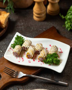 Beyaz sos, susam tohumu, kırmızı şurup ve beyaz tabakta maydanozla süslenmiş, etle dolu lezzetli gözlemeler.