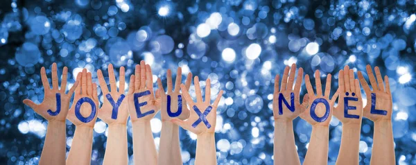 Mãos construindo Joyeux Noel significa Feliz Natal, fundo espumante Bokeh — Fotografia de Stock