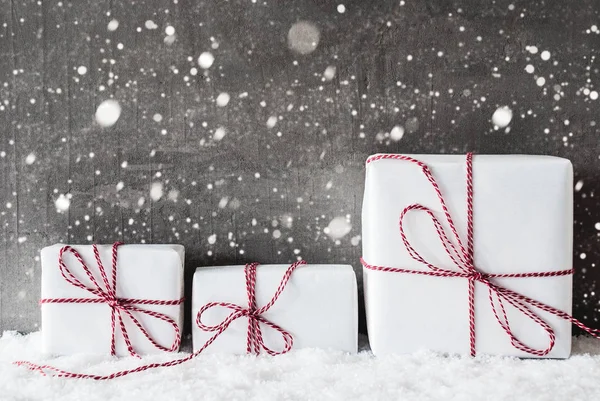 Белые подарки с красной лентой, грубый цемент задний план, снежинки — стоковое фото