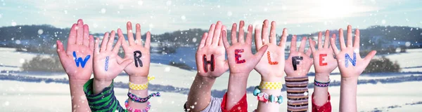 Le mani dei bambini che tengono parola Wir Helfen significa che aiutiamo, sfondo invernale nevoso — Foto Stock