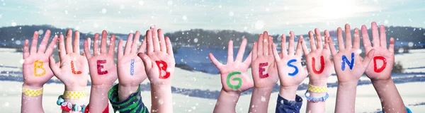 Mani dei bambini che tengono parola Bleib Gesund significa rimanere in buona salute, sfondo invernale innevato — Foto Stock