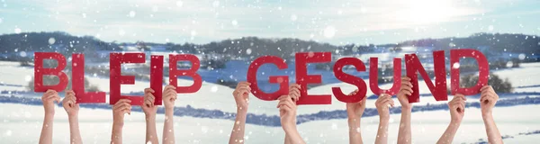 Las manos de la gente sosteniendo la palabra Bleib Gesund significa mantenerse saludable, fondo de invierno —  Fotos de Stock