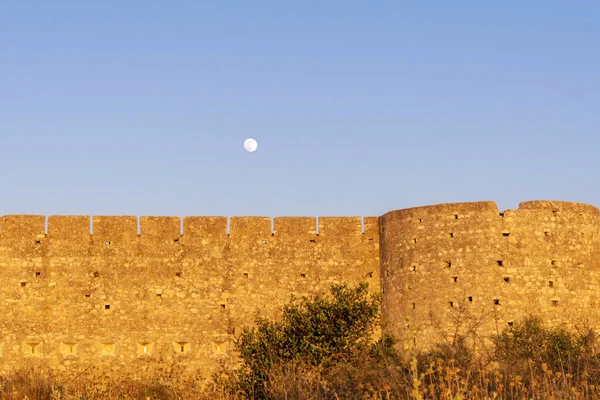 Medieval castle wall with arrow loops and battlements and fool moon above.