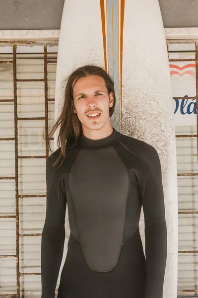 Портрет Человека Длинными Волосами Гидрокостюме Доской Серфинга Смотрящего Камеру — Бесплатное стоковое фото