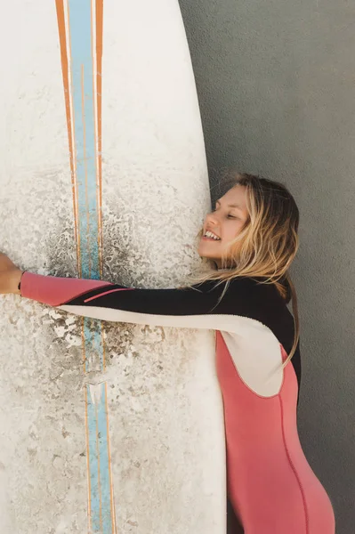 Portrait Smiling Woman Wetsuit Hugging Surfing Board Grey Wall — Stock Photo, Image