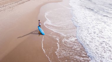 aerial view of young woman in swimsuit pulling surfboard on sandy beach, Ashdod, Israel clipart