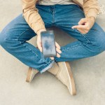 Schnappschuss von Mann, der auf Skateboard sitzt und Smartphone mit leerem Bildschirm benutzt