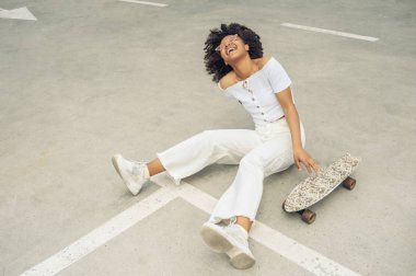 bir kaykay ile oturma ve sokakta gülüyor neşeli Afro-Amerikan kız yüksek açılı görünüş