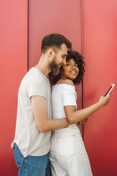 Bonito Jovem Abraçando Sorridente Namorada Usando Smartphone Rua — Fotografia de Stock