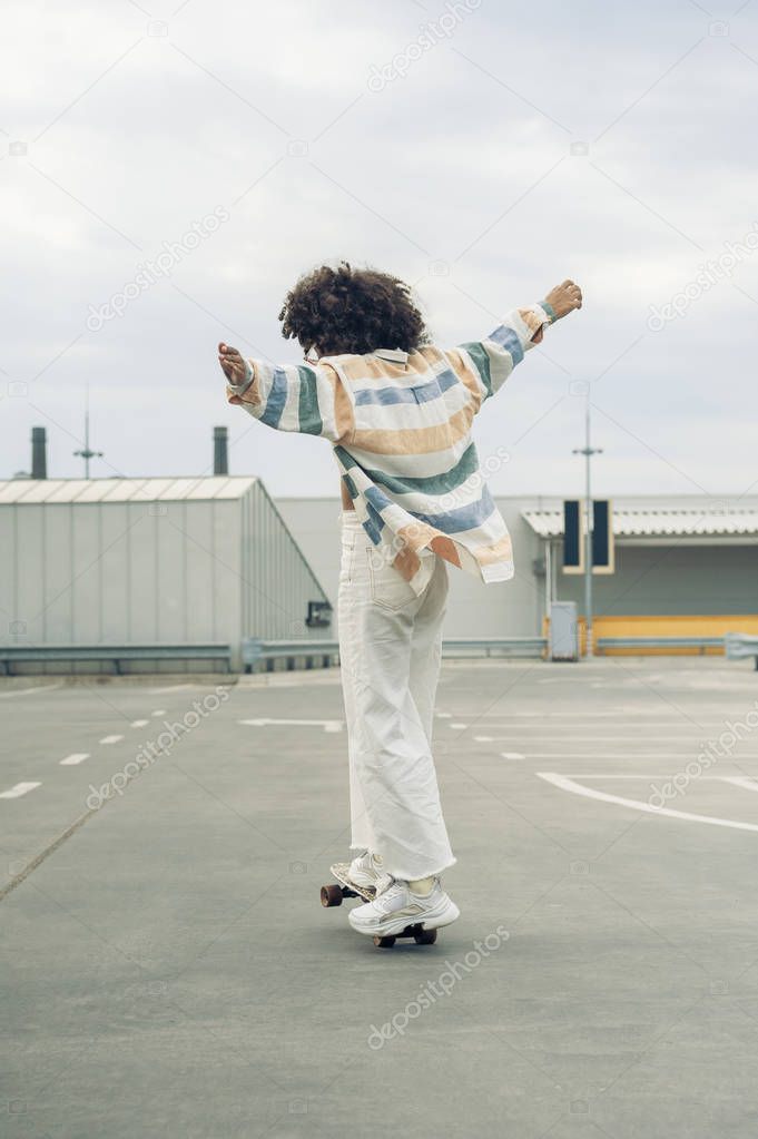 back view of young woman with open arms skateboarding on street