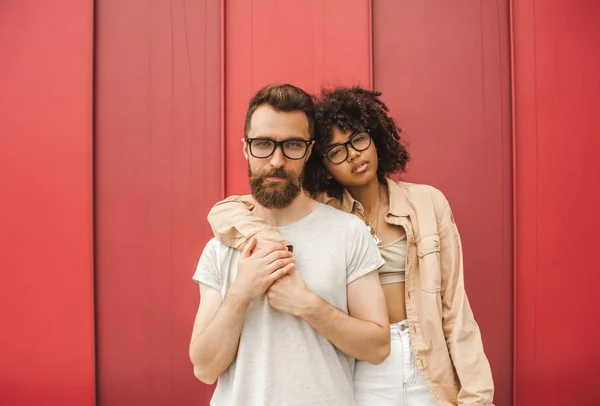 beautiful stylish young interracial couple in eyeglasses embracing and looking at camera