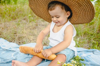battaniye piknik üzerinde oturan ve baget holding hasır şapkalı sevimli yürümeye başlayan çocuk